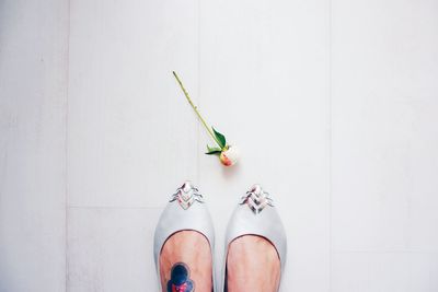 Low section of woman standing by flower bud on white floor