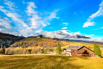 Scenic view of field by houses against sky