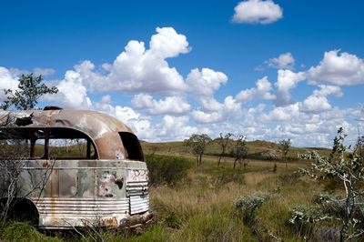 Abandoned car on field against sky