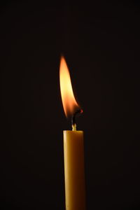 Close-up of burning candle against black background