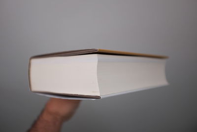 Cropped image of person balancing book on finger against white wall