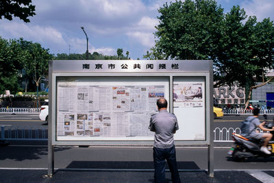 Rear view of man standing by bus against sky in city