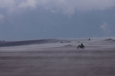 Man riding motorcycle on desert against sky