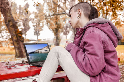 Side view of young woman using laptop on table while sitting in park