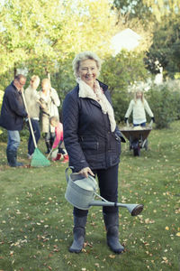 Portrait of senior woman carrying watering can while gardening with family at yard