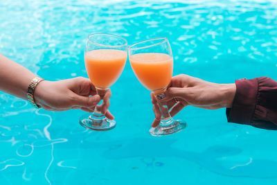 Cropped hands toasting drinks against swimming pool