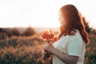 Beautiful woman standing by flowering plants on field against sky