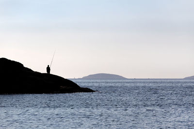 Beautiful seascape with a silhouette of a fisherman standing on rocks with fishing rod near sea