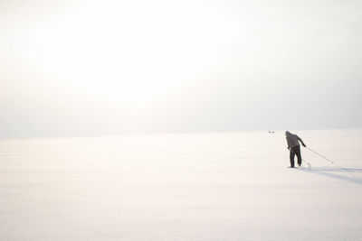 Rear view of person skiing on snow covered field against clear sky