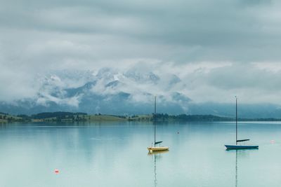 Boats in lake against cloudy sky