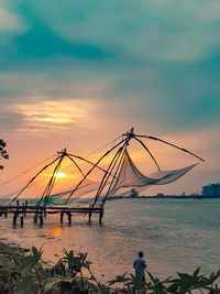 Fishing nets in sea against sky during sunset