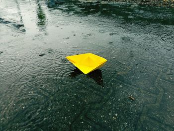 High angle view of yellow paper boat on puddle during rainy season