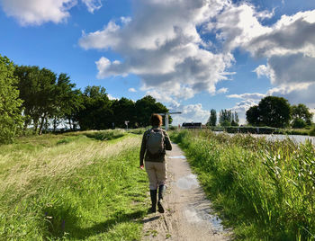 Rear view of a woman walking over a green dike along a canal in a rural summer landscape