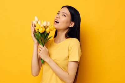 Portrait of young woman holding yellow flowers against orange background