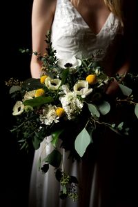 Midsection of bride holding bouquet while standing against black background