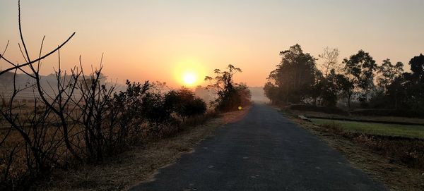 Road amidst trees against sky during sunset