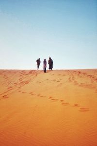 People standing on sand dune against clear sky