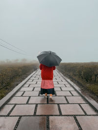 Rear view of woman walking on road during rainy season