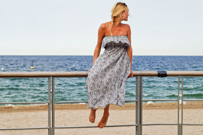 Full length on young woman sitting on railing at beach