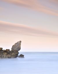 Rock formation in sea against sky at sunset