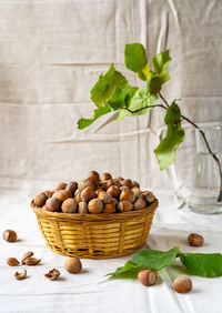 Hazelnuts in basket with leaves and tree branch on linen table cloth