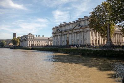 Buildings at waterfront against cloudy sky