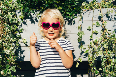 Happy cheerful child in summer sunglasses smiles looking at the camera and shows like with fingers.