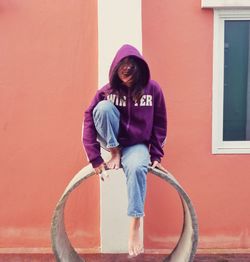 Portrait of young woman sitting against wall