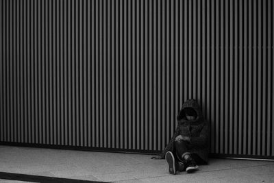 Young woman sitting on footpath against wall