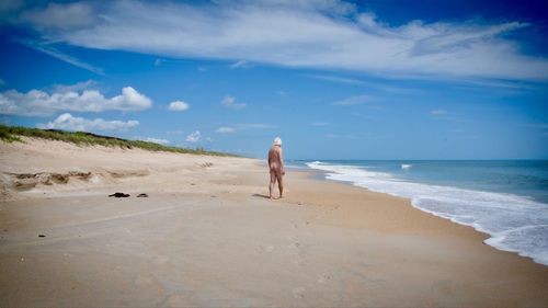 Rear view of man walking at  nude beach against sky