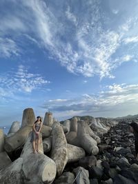 Woman standing on rock under cloudy sky