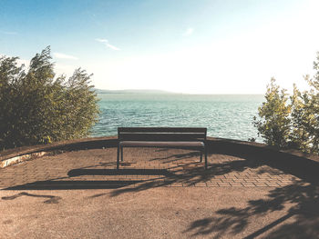 Empty bench by trees against sky