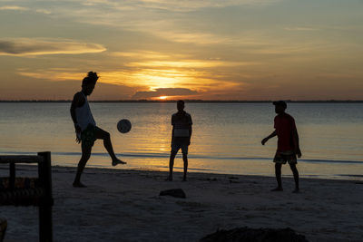 Silhouette people playing on beach against sky during sunset