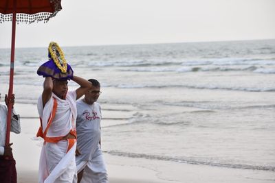 Rear view of men standing at beach against sky