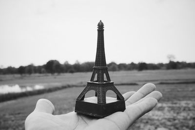 Cropped hand holding replica eiffel tower on landscape