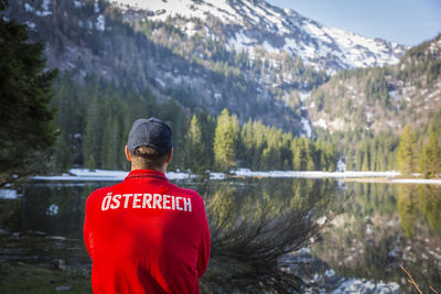 Rear view of man standing by lake against mountain