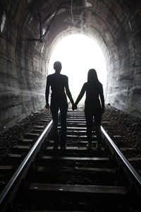 Rear view of silhouette people walking on railroad track