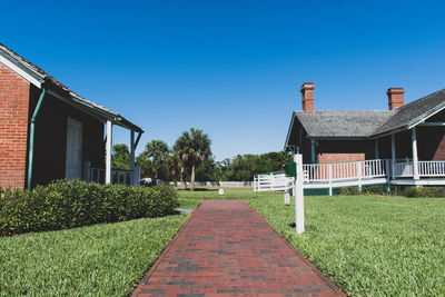 Footpath amidst houses on field against clear blue sky