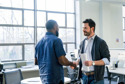 Businessmen doing handshake while standing in office