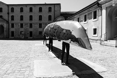 People with boat standing on footpath against buildings