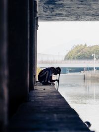 Man sitting on pier against sky