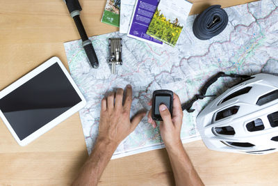 Cropped hands of man holding mobile phone over map with digital tablet and helmet on table