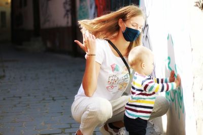 Rear view of mother wearing coronavirus mask with baby boy on street