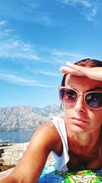 Woman in sunglasses shielding eyes at beach against sky