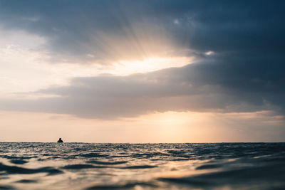 Person swimming in sea against sky during sunset