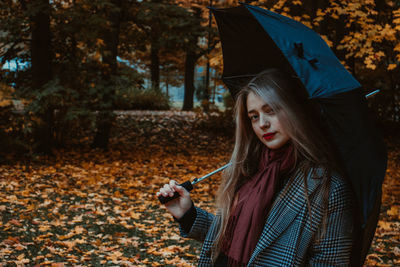 Portrait of woman holding umbrella while standing against trees in forest