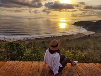 Rear view of woman sitting on beach during sunset
