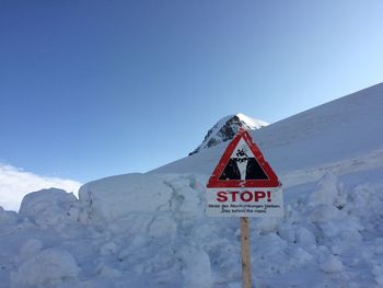 Road sign on snowcapped mountain against clear blue sky