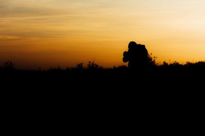 Silhouette man photographer standing against orange sky during sunset