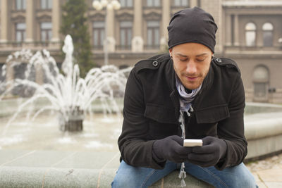 Young man sitting in city during winter